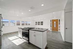 Kitchen featuring gas stove, white cabinetry, a center island, and dark wood-type flooring