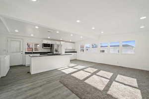 Kitchen with appliances with stainless steel finishes, tasteful backsplash, washing machine and dryer, dark hardwood / wood-style floors, and white cabinetry