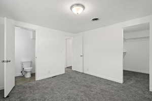 Unfurnished bedroom with ensuite bath, a spacious closet, a closet, and dark colored carpet