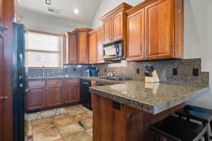 Kitchen featuring black appliances, a breakfast bar, lofted ceiling, and backsplash