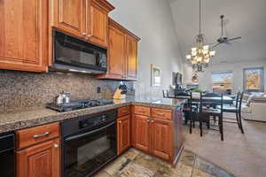 Kitchen featuring light carpet, high vaulted ceiling, black appliances, ceiling fan with notable chandelier, and tasteful backsplash