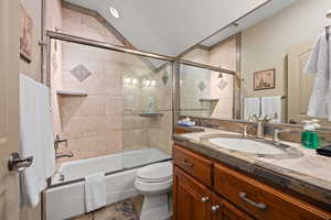 Full bathroom with vanity, lofted ceiling, tile patterned floors, bath / shower combo with glass door, and toilet