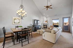 Carpeted living room featuring a tile fireplace, ceiling fan with notable chandelier, and high vaulted ceiling