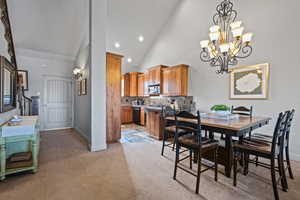 Dining space featuring a chandelier, high vaulted ceiling, and light colored carpet