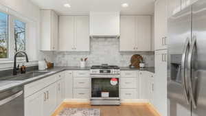 Kitchen featuring sink, light hardwood / wood-style flooring, tasteful backsplash, white cabinetry, and stainless steel appliances