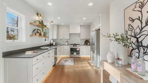 Kitchen featuring white cabinetry, sink, stainless steel appliances, tasteful backsplash, and light hardwood / wood-style floors