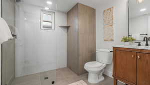 Bathroom featuring tile patterned floors, vanity, tiled shower, and toilet