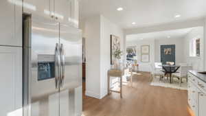 Kitchen with stainless steel fridge with ice dispenser, light hardwood / wood-style floors, and white cabinetry