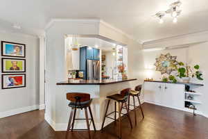 Kitchen featuring dark hardwood / wood-style floors, blue cabinetry, kitchen peninsula, a breakfast bar area, and stainless steel refrigerator