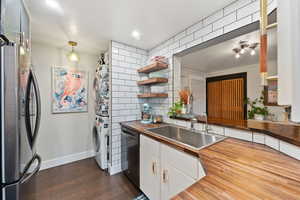 Kitchen featuring wooden counters, sink, stacked washing maching and dryer, appliances with stainless steel finishes, and white cabinetry