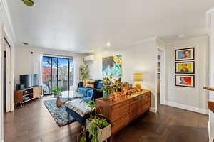 Living room with dark hardwood / wood-style floors, ornamental molding, and a wall mounted AC