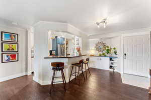 Kitchen with ornamental molding, dark hardwood / wood-style flooring, a kitchen bar, kitchen peninsula, and stainless steel refrigerator