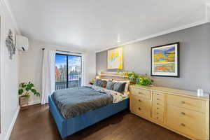 Bedroom with a wall mounted air conditioner, dark hardwood / wood-style floors, access to exterior, and crown molding