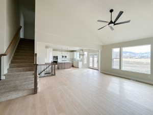 Unfurnished living room featuring light wood-type flooring, ceiling fan, stairs, and high vaulted ceiling