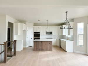 Kitchen with white cabinets, appliances with stainless steel finishes, a center island, hanging light fixtures, and light countertops