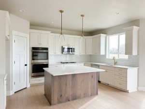 Kitchen featuring a kitchen island, appliances with stainless steel finishes, light countertops, and pendant lighting