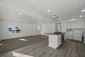 Kitchen with separate washer and dryer, white cabinetry, stainless steel range with gas cooktop, and wood-type flooring