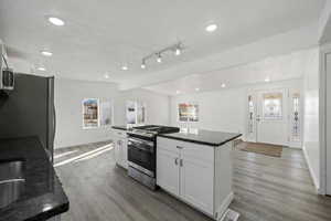 Kitchen featuring wood-type flooring, white cabinetry, a kitchen island, and stainless steel gas range