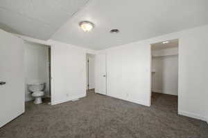 Unfurnished bedroom with ensuite bathroom, dark carpet, a walk in closet, and a closet