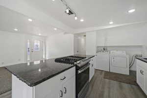 Kitchen with washing machine and dryer, white cabinets, dark wood-type flooring, and stainless steel gas range