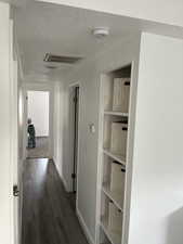 Hallway with a textured ceiling, visible vents, dark wood-style flooring, and baseboards