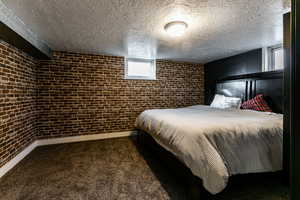 Carpeted bedroom featuring a textured ceiling and brick wall