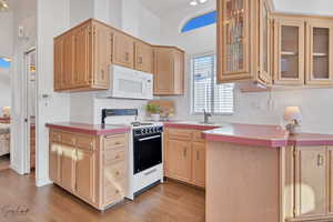 Kitchen featuring white appliances, sink, light brown cabinetry, and light hardwood / wood-style flooring