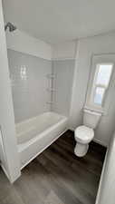 Bathroom with hardwood / wood-style flooring, toilet, and tiled shower / bath