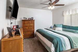 Bedroom featuring dark colored carpet, ceiling fan, and a textured ceiling