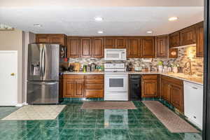 Kitchen with white appliances, backsplash, dark tile patterned floors, and sink