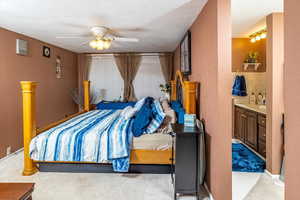 Bedroom featuring ceiling fan, ensuite bathroom, and a textured ceiling