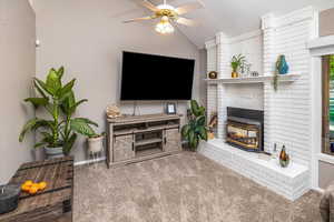 Living room featuring carpet, lofted ceiling, ceiling fan, a fireplace, and a textured ceiling