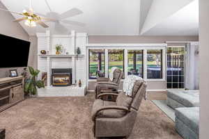 Carpeted living room featuring a brick fireplace, ceiling fan, and vaulted ceiling