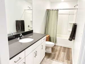 Full bathroom featuring hardwood / wood-style flooring, vanity, toilet, and shower / tub combo with curtain