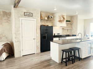 Kitchen featuring black fridge with ice dispenser, gas range, sink, white cabinetry, and a breakfast bar area