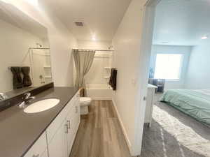 Full bathroom with hardwood / wood-style floors, a textured ceiling, toilet, vanity, and shower / tub combo