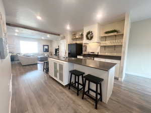 Kitchen featuring a breakfast bar area, black fridge with ice dispenser, white cabinets, and hardwood / wood-style flooring