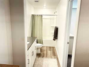 Full bathroom with vanity, toilet, wood-type flooring, and shower / bath combo with shower curtain