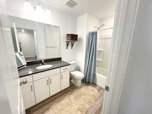 Full bathroom with shower / bath combination with curtain, vanity, hardwood / wood-style flooring, and toilet