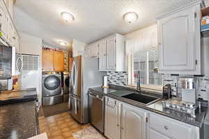 Kitchen featuring separate washer and dryer, sink, white cabinets, decorative backsplash, and stainless steel appliances