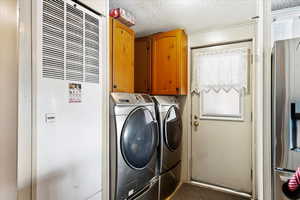 Clothes washing area featuring cabinets, a textured ceiling, and independent washer and dryer