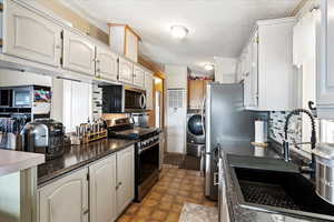 Kitchen featuring washer / clothes dryer, white cabinetry, sink, and appliances with stainless steel finishes