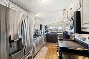 Kitchen featuring lofted ceiling, sink, appliances with stainless steel finishes, a textured ceiling, and white cabinets