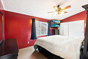 Bedroom with carpet flooring, ceiling fan, lofted ceiling, and a textured ceiling