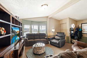 Living room with lofted ceiling with beams, carpet flooring, and a textured ceiling