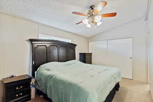 Bedroom featuring lofted ceiling, ceiling fan, a textured ceiling, light colored carpet, and a closet