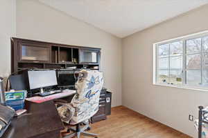 Office space with vaulted ceiling, light hardwood / wood-style floors, and a textured ceiling