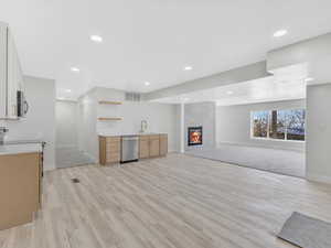 Kitchen featuring a tile fireplace, sink, appliances with stainless steel finishes, and light hardwood / wood-style flooring