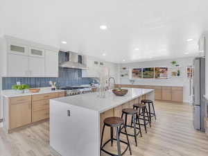 Kitchen with a large island with sink, light hardwood / wood-style flooring, white cabinetry, and wall chimney range hood