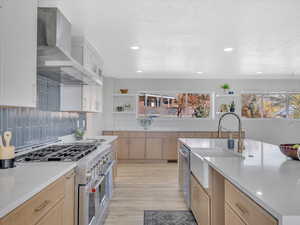 Kitchen featuring light brown cabinets, wall chimney exhaust hood, light wood-type flooring, and appliances with stainless steel finishes